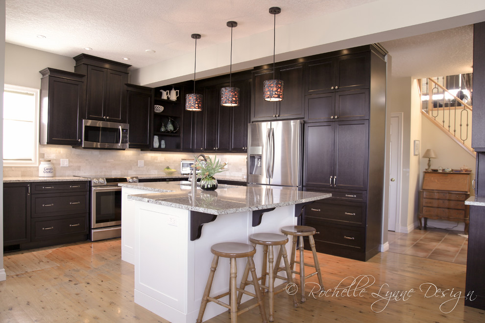 Inspiration for a mid-sized transitional l-shaped light wood floor eat-in kitchen remodel in Calgary with an undermount sink, recessed-panel cabinets, dark wood cabinets, granite countertops, beige backsplash, stone tile backsplash, stainless steel appliances and an island