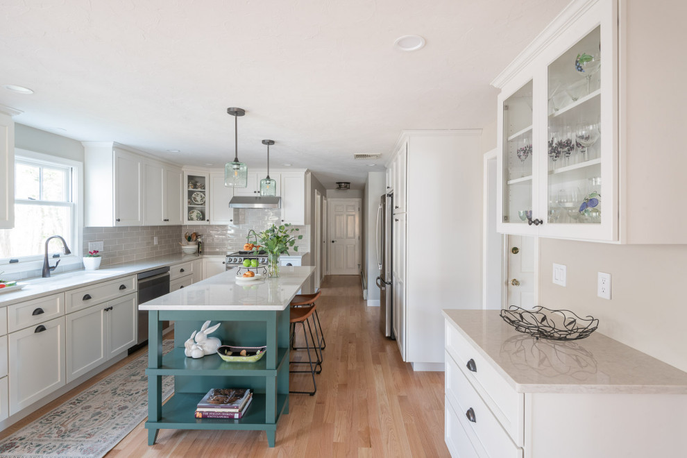 Example of a large transitional galley light wood floor and brown floor eat-in kitchen design in Boston with an undermount sink, shaker cabinets, white cabinets, quartz countertops, beige backsplash, ceramic backsplash, stainless steel appliances, an island and white countertops