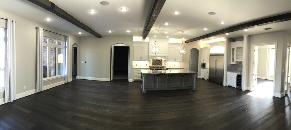 Mid-sized transitional l-shaped dark wood floor and brown floor open concept kitchen photo in Orange County with a farmhouse sink, raised-panel cabinets, white cabinets, marble countertops, metallic backsplash, metal backsplash, stainless steel appliances and an island