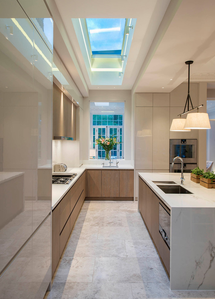 Photo of a large transitional l-shaped eat-in kitchen in London with a drop-in sink, flat-panel cabinets, medium wood cabinets, marble benchtops, white splashback, marble splashback, stainless steel appliances, ceramic floors, with island, grey floor and white benchtop.