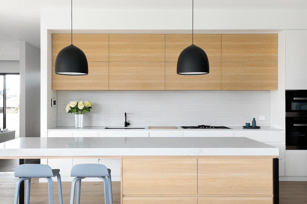 Inspiration for a contemporary galley eat-in kitchen in Canberra - Queanbeyan with an undermount sink, quartz benchtops, white splashback, mosaic tile splashback, black appliances, light hardwood floors, with island, white benchtop, flat-panel cabinets, light wood cabinets and beige floor.