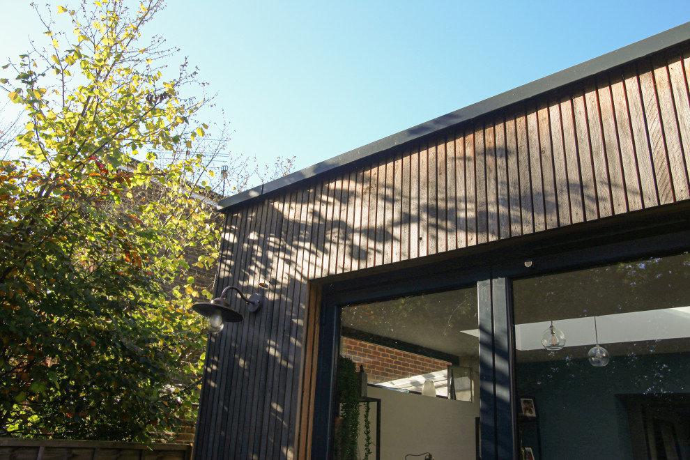 Cette image montre une petite façade de maison design en bois et planches et couvre-joints de plain-pied avec un toit plat, un toit mixte et un toit gris.