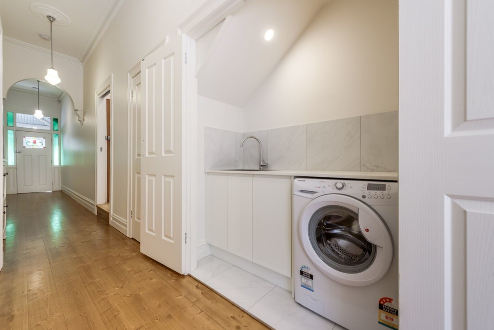 Small modern galley utility room in Melbourne with a drop-in sink, louvered cabinets, white cabinets, granite benchtops, white walls, ceramic floors, an integrated washer and dryer, white floor and white benchtop.
