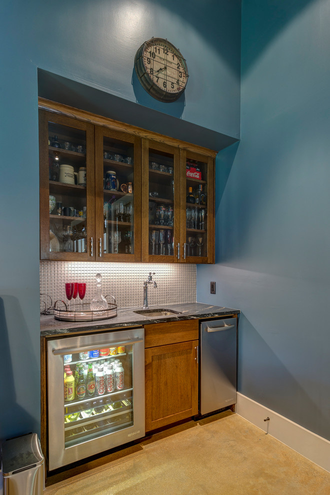 Design ideas for a small country single-wall wet bar in Austin with an undermount sink, shaker cabinets, medium wood cabinets, soapstone benchtops, grey splashback, glass tile splashback, concrete floors, black benchtop and beige floor.