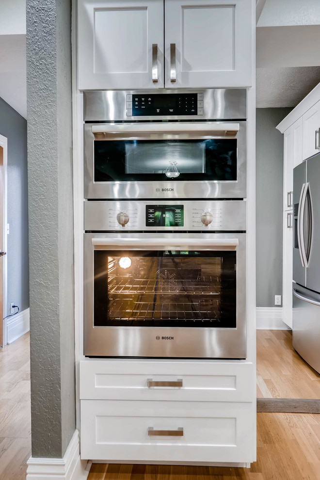 Inspiration for a large rustic light wood floor and brown floor eat-in kitchen remodel in Denver with a farmhouse sink, shaker cabinets, white cabinets, quartz countertops, white backsplash, ceramic backsplash, stainless steel appliances, a peninsula and brown countertops