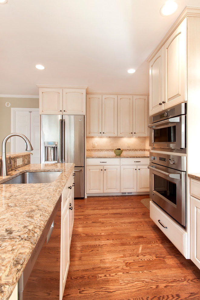Elegant u-shaped medium tone wood floor eat-in kitchen photo in DC Metro with raised-panel cabinets, quartz countertops, beige backsplash, stainless steel appliances and an island