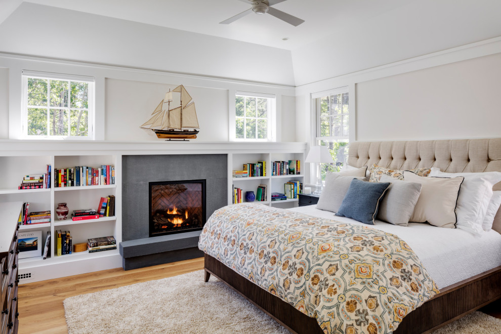 This is an example of a transitional master bedroom in Boston with white walls, medium hardwood floors, a standard fireplace, a concrete fireplace surround and brown floor.