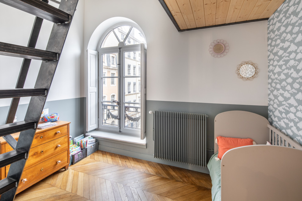 Photo of a small traditional gender neutral children’s room in Lyon with blue walls, light hardwood flooring, brown floors and wallpapered walls.