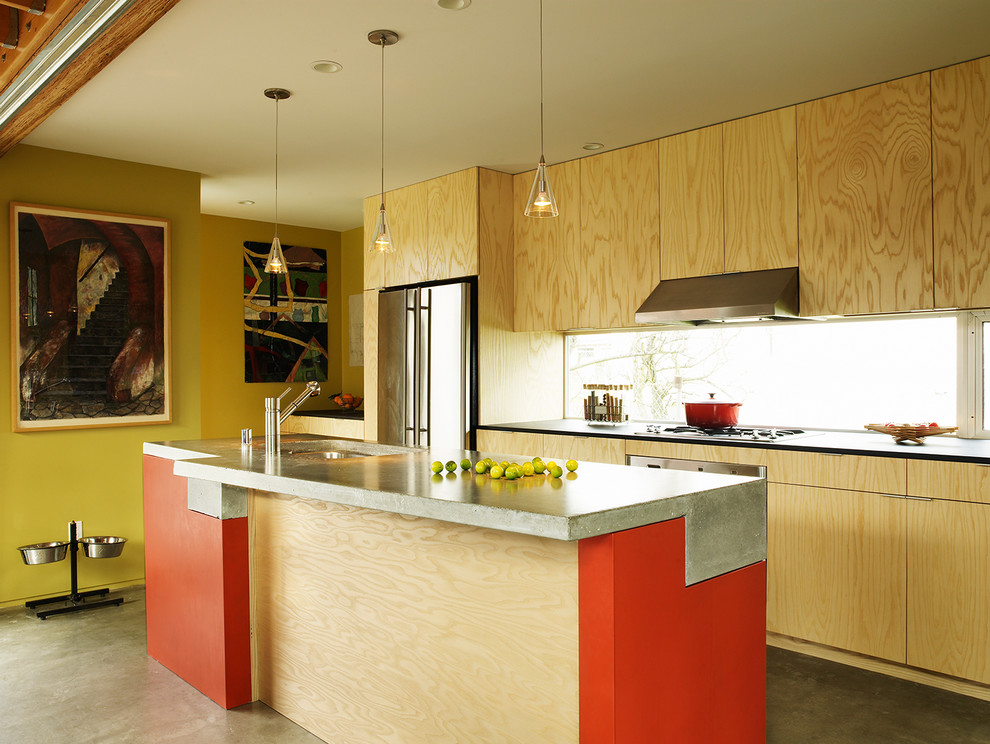 This is an example of an industrial galley kitchen in Seattle with a single-bowl sink, flat-panel cabinets, light wood cabinets, concrete benchtops, stainless steel appliances, concrete floors and with island.