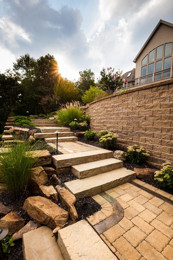 This is an example of a large traditional sloped full sun garden in Other with a retaining wall and concrete pavers.