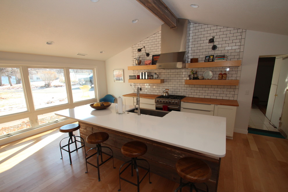 This is an example of a large country galley open plan kitchen in Other with a farmhouse sink, flat-panel cabinets, white cabinets, quartz benchtops, white splashback, subway tile splashback, stainless steel appliances, medium hardwood floors and with island.