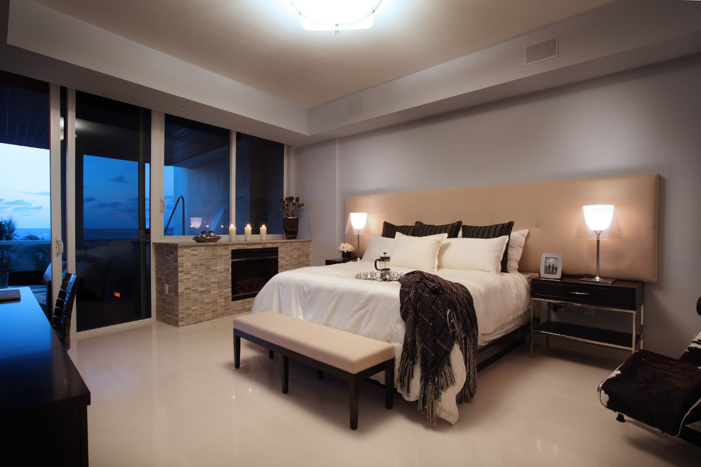 This is an example of a mid-sized contemporary master bedroom in Miami with beige walls, a standard fireplace, a stone fireplace surround, marble floors and white floor.