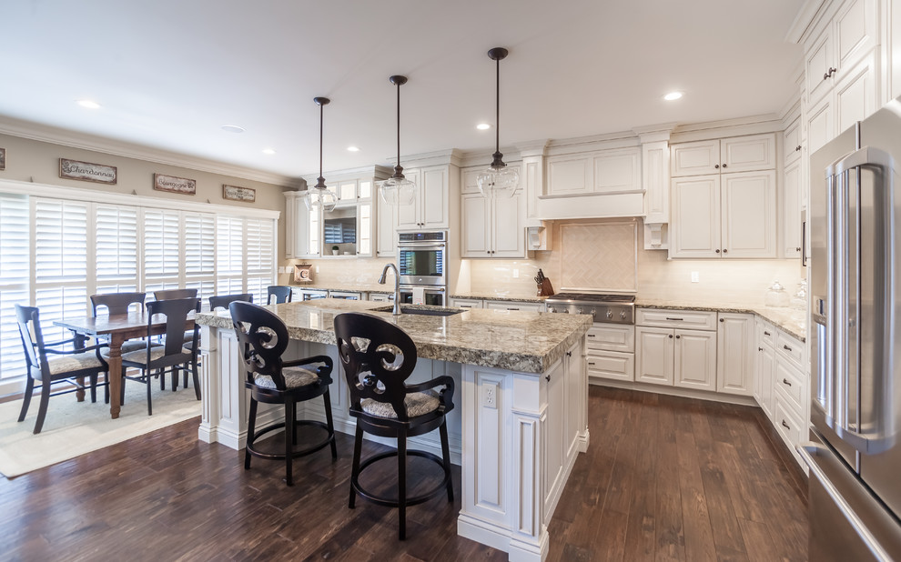 Example of a large transitional l-shaped kitchen design in St Louis with an undermount sink, raised-panel cabinets, white cabinets, granite countertops, beige backsplash, subway tile backsplash, stainless steel appliances and an island