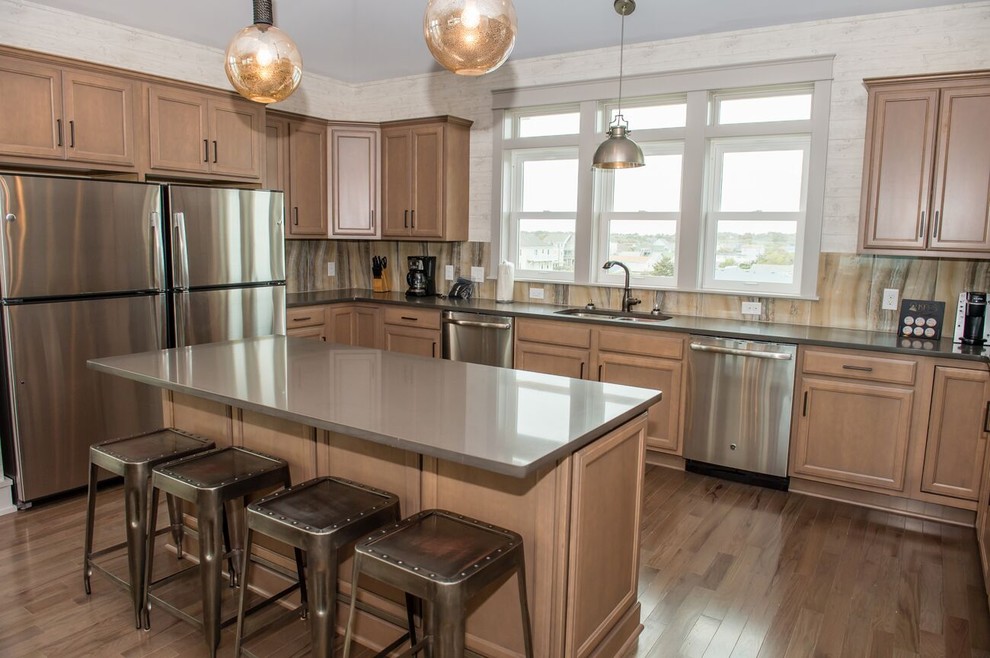 Example of a mid-sized transitional u-shaped medium tone wood floor eat-in kitchen design with a double-bowl sink, recessed-panel cabinets, medium tone wood cabinets, solid surface countertops, beige backsplash, stone slab backsplash, stainless steel appliances and an island