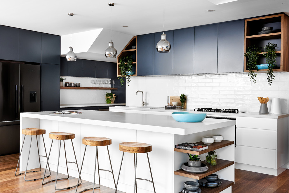 Design ideas for a mid-sized beach style kitchen in Sydney with a double-bowl sink, flat-panel cabinets, quartz benchtops, white splashback, with island, white benchtop, subway tile splashback, black cabinets, black appliances and medium hardwood floors.