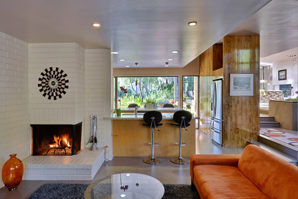 This is an example of a mid-sized midcentury open concept family room in San Diego with white walls, medium hardwood floors, a corner fireplace and a brick fireplace surround.
