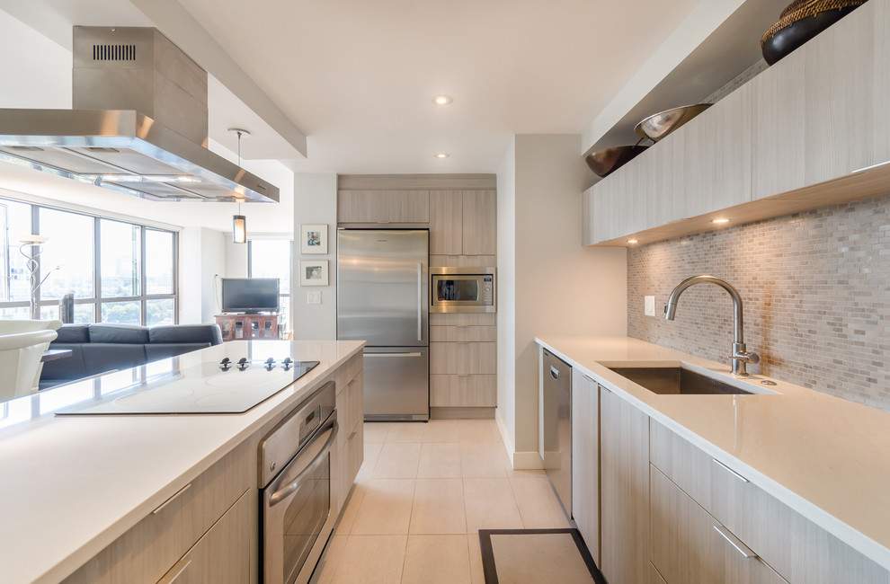 This is an example of a contemporary l-shaped open plan kitchen in Vancouver with a single-bowl sink, flat-panel cabinets, beige cabinets, beige splashback, matchstick tile splashback, stainless steel appliances, with island, beige floor and beige benchtop.