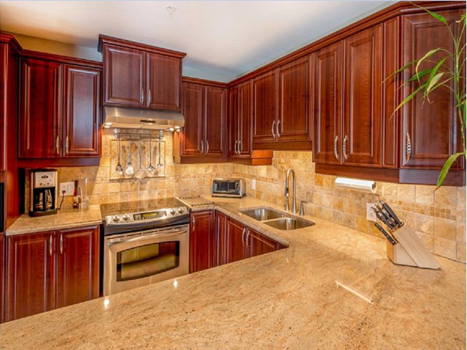 Photo of a mid-sized traditional u-shaped eat-in kitchen in Detroit with a double-bowl sink, raised-panel cabinets, dark wood cabinets, granite benchtops, beige splashback, travertine splashback, stainless steel appliances, travertine floors, a peninsula and beige floor.