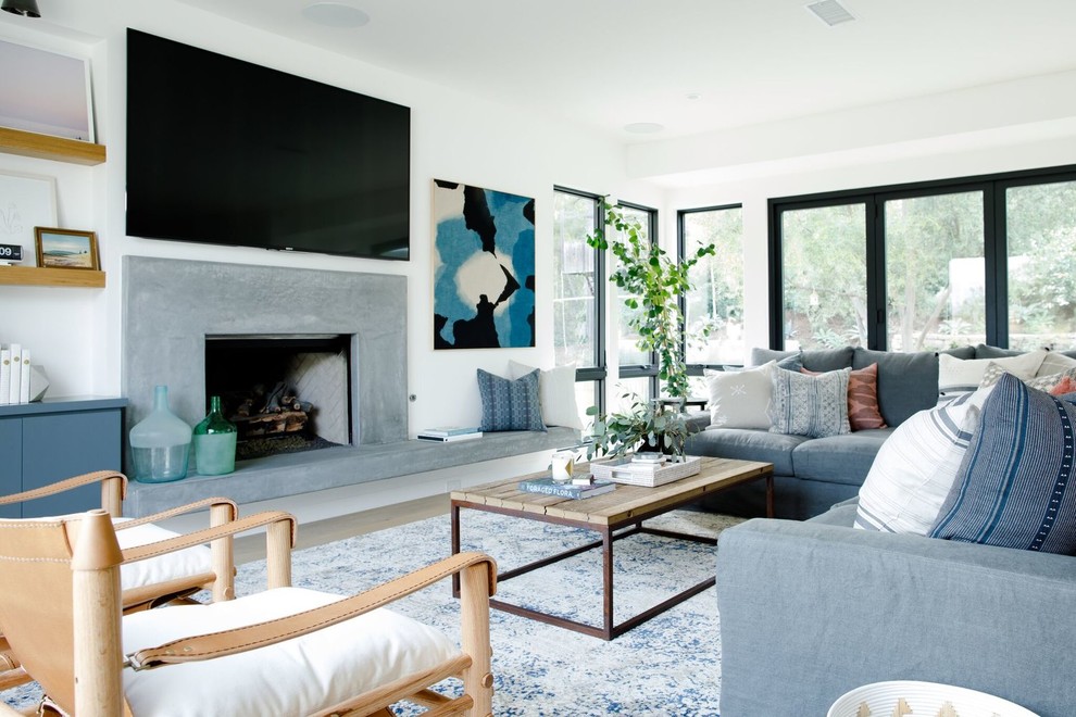 Inspiration for a large contemporary open concept living room in Salt Lake City with white walls, a standard fireplace, a concrete fireplace surround, a wall-mounted tv, light hardwood floors and grey floor.