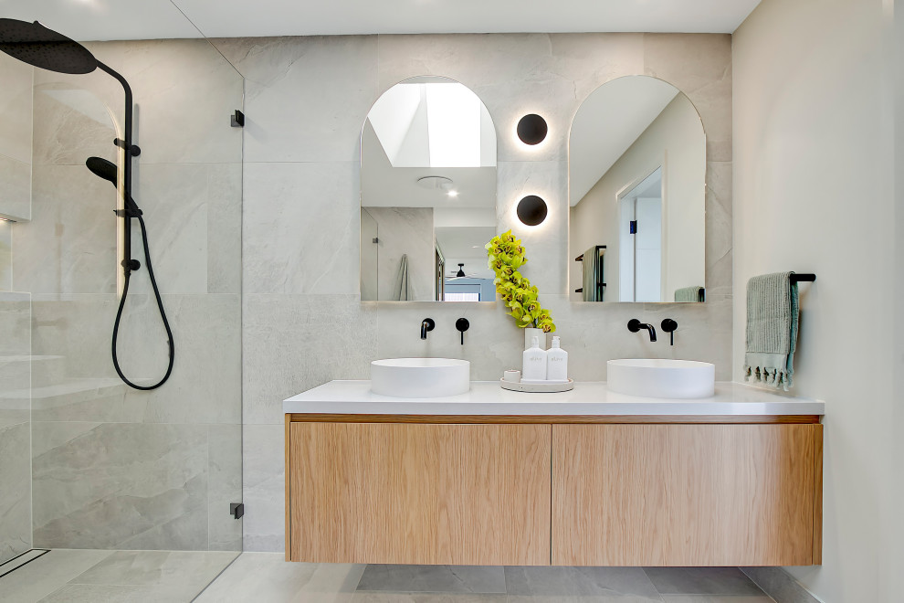 Пример оригинального дизайна: большая главная ванная комната в стиле модернизм с плоскими фасадами, фасадами цвета дерева среднего тона, двойным душем, унитазом-моноблоком, серой плиткой, керамогранитной плиткой, серыми стенами, полом из керамогранита, настольной раковиной, столешницей из искусственного кварца, серым полом, открытым душем, белой столешницей, нишей, тумбой под две раковины и подвесной тумбой