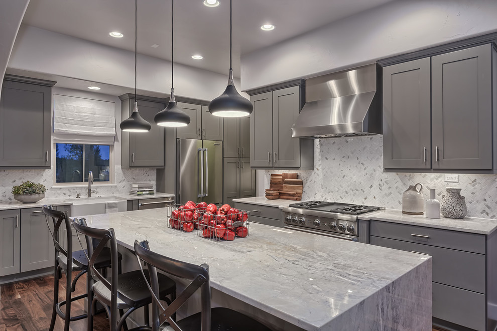 Photo of a transitional l-shaped kitchen in Denver with a farmhouse sink, shaker cabinets, grey cabinets, white splashback, mosaic tile splashback, stainless steel appliances, dark hardwood floors and with island.