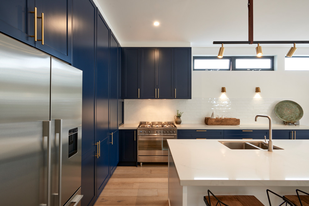 Inspiration for an expansive beach style l-shaped open plan kitchen in Sydney with shaker cabinets, blue cabinets, quartz benchtops, subway tile splashback, with island, an undermount sink, white splashback, stainless steel appliances, light hardwood floors, brown floor and white benchtop.
