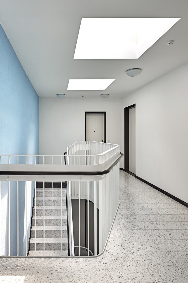 Réalisation d'un grand couloir minimaliste avec un mur bleu, un sol en terrazzo et un sol gris.