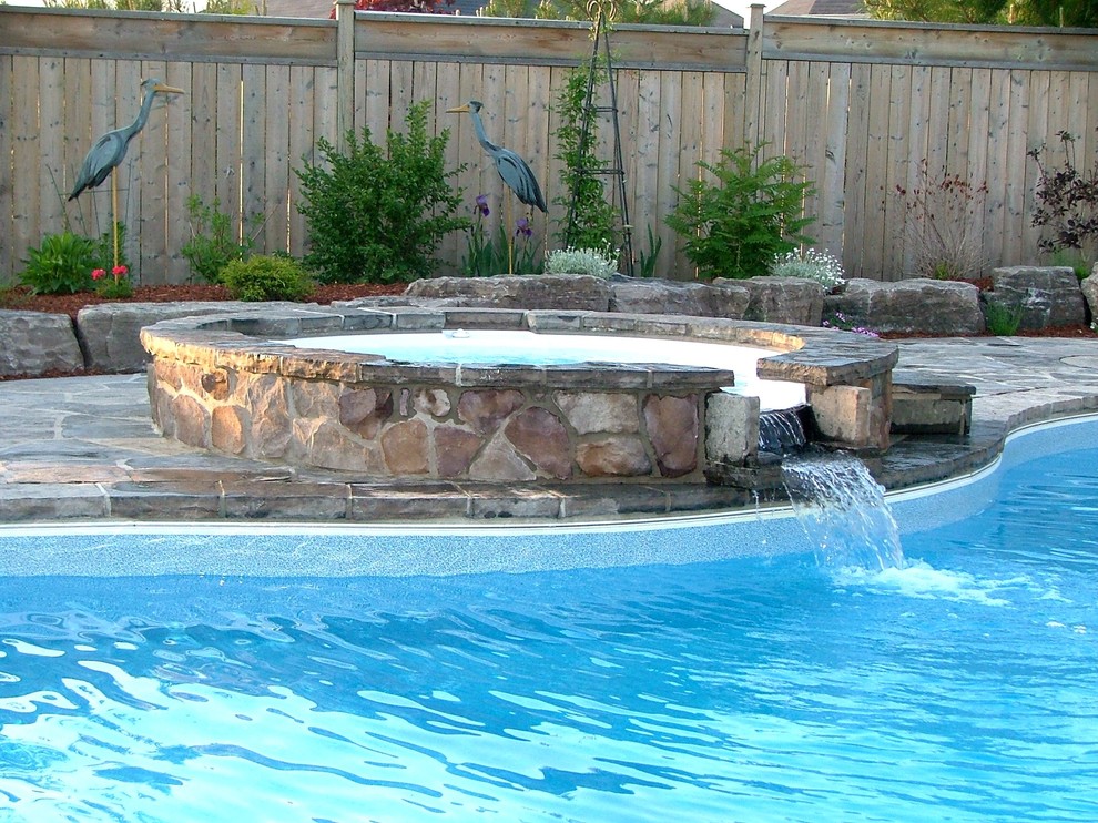 This is an example of a large traditional backyard custom-shaped aboveground pool in Toronto with a hot tub and natural stone pavers.