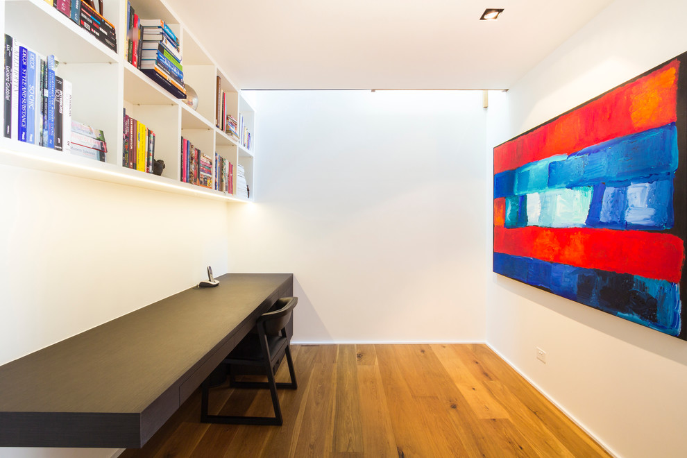 This is an example of a contemporary study room in Sydney with white walls, medium hardwood floors and a built-in desk.