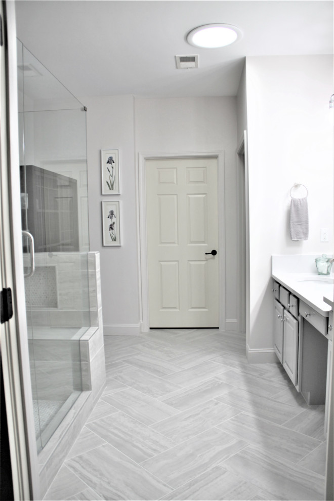 Exemple d'une grande salle de bain principale chic avec un placard avec porte à panneau surélevé, des portes de placard grises, une douche ouverte, WC à poser, un carrelage gris, des carreaux de porcelaine, un mur blanc, un sol en carrelage de porcelaine, un lavabo encastré, un plan de toilette en quartz modifié, un sol gris, une cabine de douche à porte battante, un plan de toilette blanc, un banc de douche, meuble double vasque et meuble-lavabo encastré.