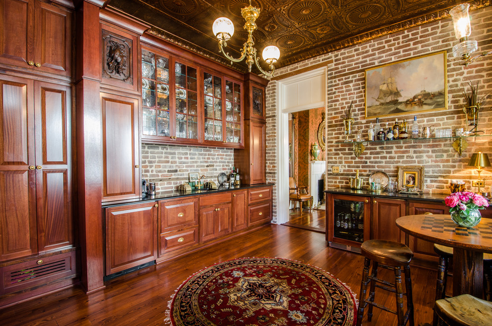 This is an example of a large traditional l-shaped wet bar in Charleston with an undermount sink, raised-panel cabinets, dark wood cabinets and dark hardwood floors.