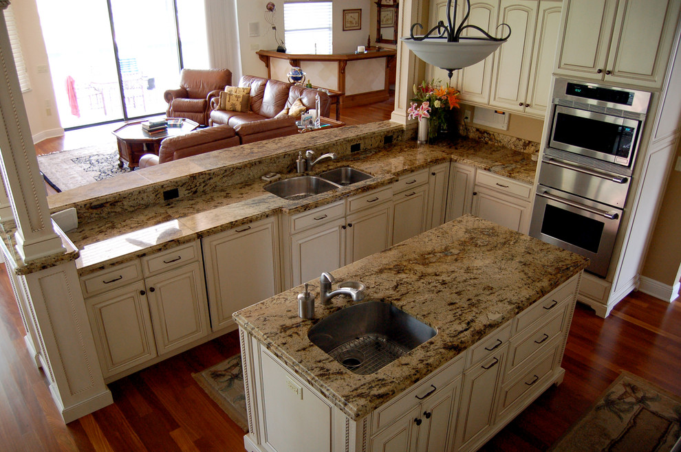 Design ideas for a traditional l-shaped open plan kitchen in Tampa with an undermount sink, raised-panel cabinets, white cabinets, granite benchtops, stainless steel appliances, medium hardwood floors, with island, beige splashback and brown floor.