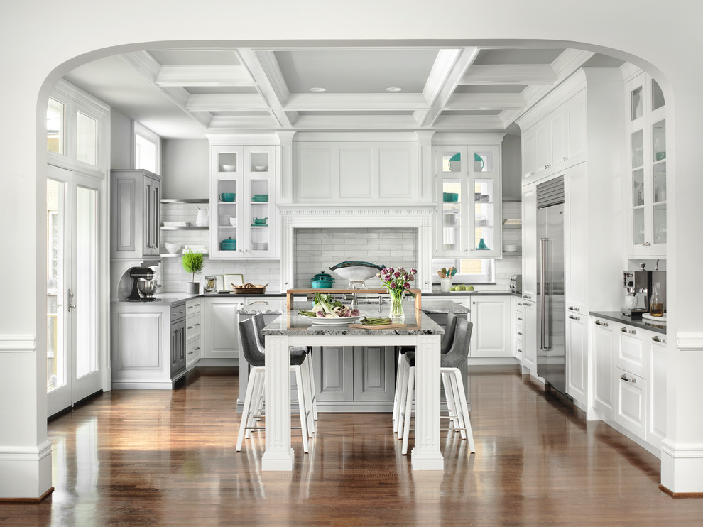 Photo of a traditional u-shaped eat-in kitchen in St Louis with raised-panel cabinets, white cabinets, grey splashback, stainless steel appliances, medium hardwood floors, with island, brown floor and grey benchtop.