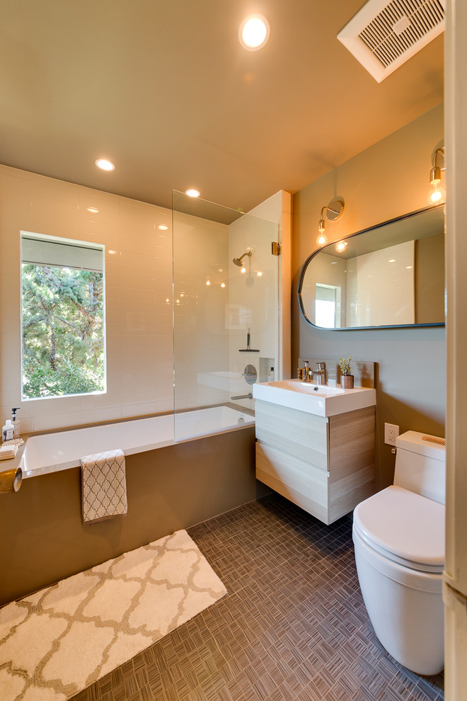 This is an example of a large contemporary bathroom in San Francisco with flat-panel cabinets, light wood cabinets, a drop-in tub, a shower/bathtub combo, a one-piece toilet, white tile, brown walls and a wall-mount sink.
