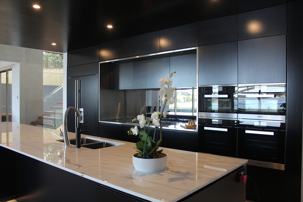 This is an example of a large contemporary galley open plan kitchen in Sydney with an undermount sink, flat-panel cabinets, black cabinets, marble benchtops, mirror splashback, stainless steel appliances, limestone floors, with island and grey floor.