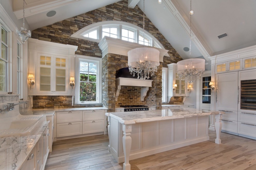 Example of a large classic u-shaped light wood floor eat-in kitchen design in Dallas with a farmhouse sink, recessed-panel cabinets, white cabinets, marble countertops, multicolored backsplash, stone tile backsplash, paneled appliances and an island