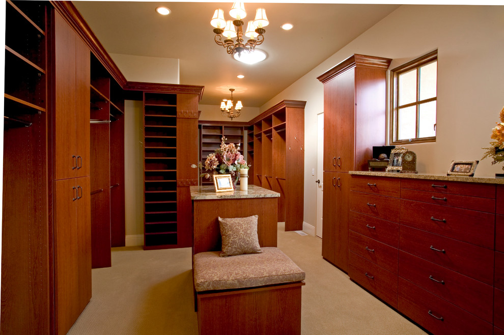 Photo of a mid-sized mediterranean gender-neutral walk-in wardrobe in Other with flat-panel cabinets, dark wood cabinets, carpet and beige floor.