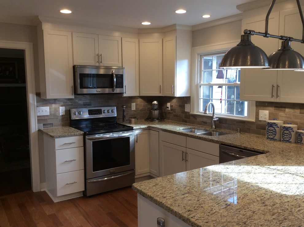 Example of a transitional u-shaped medium tone wood floor kitchen design with an undermount sink, shaker cabinets, white cabinets, granite countertops, beige backsplash, subway tile backsplash, stainless steel appliances and a peninsula