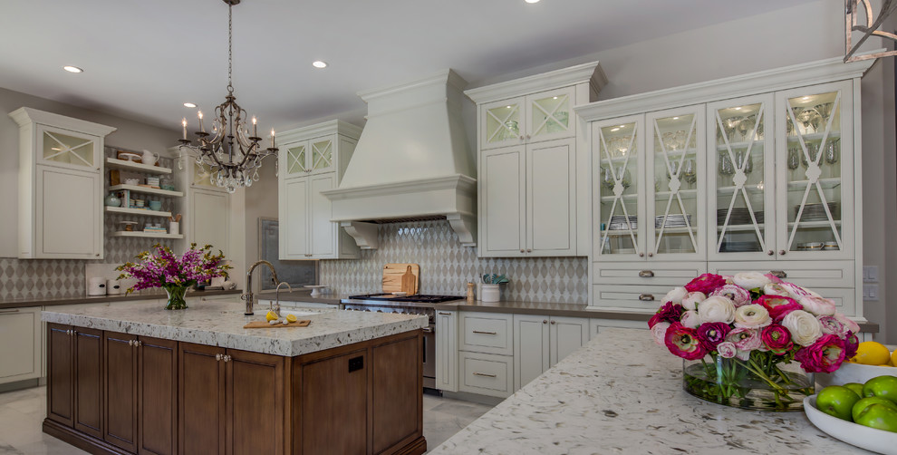 Large transitional l-shaped marble floor and white floor eat-in kitchen photo in Phoenix with a drop-in sink, glass-front cabinets, white cabinets, granite countertops, beige backsplash, ceramic backsplash, stainless steel appliances and two islands