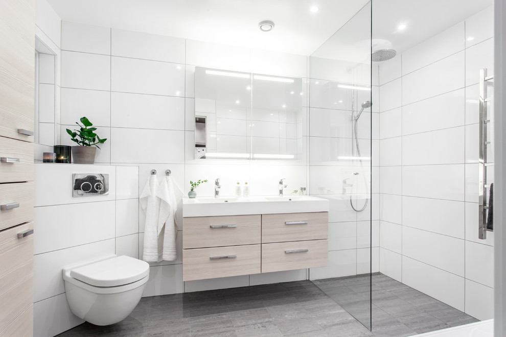 Design ideas for a large contemporary master bathroom in Gothenburg with flat-panel cabinets, light wood cabinets, an alcove shower, a one-piece toilet, porcelain tile, white walls, limestone floors, a drop-in sink, white tile, grey floor and an open shower.