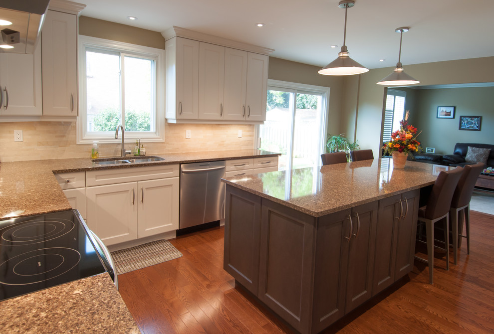 Example of a large transitional u-shaped medium tone wood floor and brown floor enclosed kitchen design in Toronto with a double-bowl sink, shaker cabinets, white cabinets, granite countertops, beige backsplash, ceramic backsplash, stainless steel appliances and an island