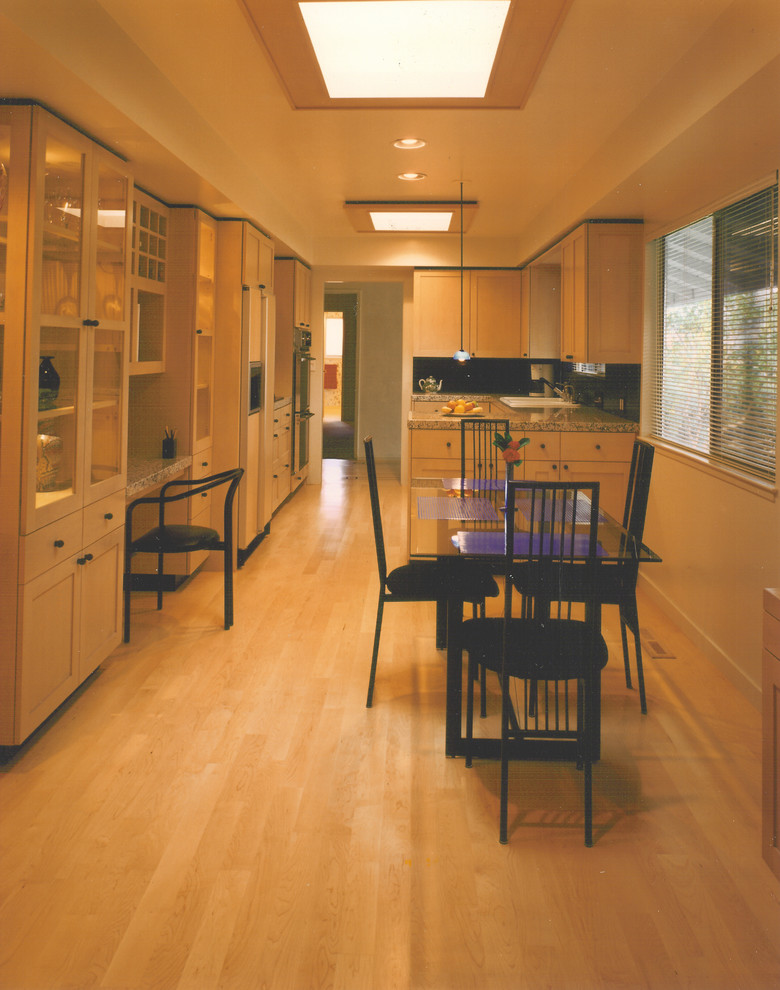This is an example of a large modern galley eat-in kitchen in San Francisco with a double-bowl sink, shaker cabinets, light wood cabinets, granite benchtops, black splashback, panelled appliances, light hardwood floors, stone slab splashback, a peninsula and yellow floor.
