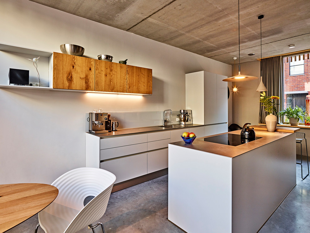 Photo of a mid-sized contemporary galley eat-in kitchen in Amsterdam with an integrated sink, flat-panel cabinets, grey cabinets, stainless steel benchtops, white splashback, glass sheet splashback, stainless steel appliances, concrete floors, with island and grey floor.