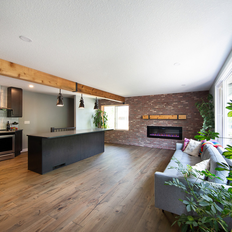 Small industrial open concept living room in Edmonton with green walls, medium hardwood floors, a standard fireplace, a brick fireplace surround, a wall-mounted tv and brown floor.
