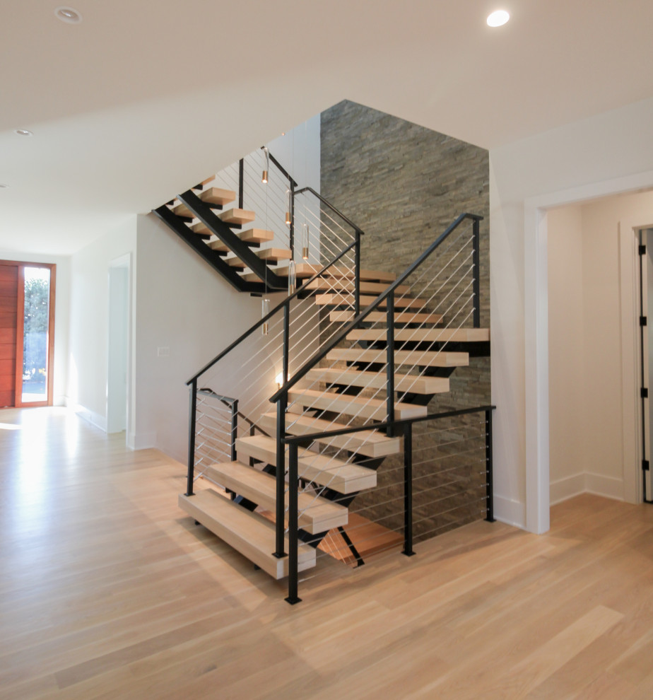 Пример оригинального дизайна: большая лестница на больцах в стиле фьюжн с деревянными ступенями, металлическими перилами и кирпичными стенами