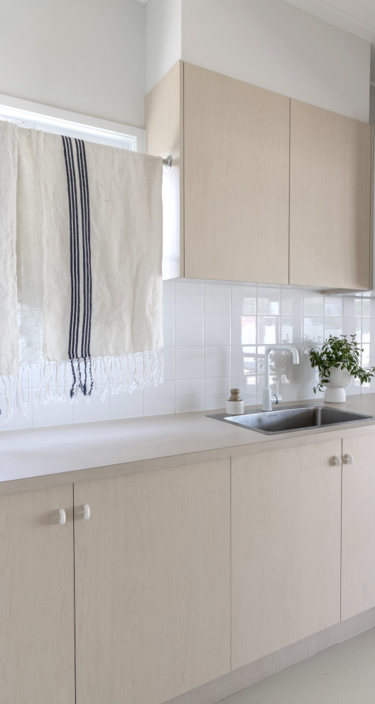 Idéer för stora minimalistiska parallella tvättstugor enbart för tvätt, med en enkel diskho, släta luckor, skåp i ljust trä, laminatbänkskiva, vitt stänkskydd, stänkskydd i keramik och en tvättpelare