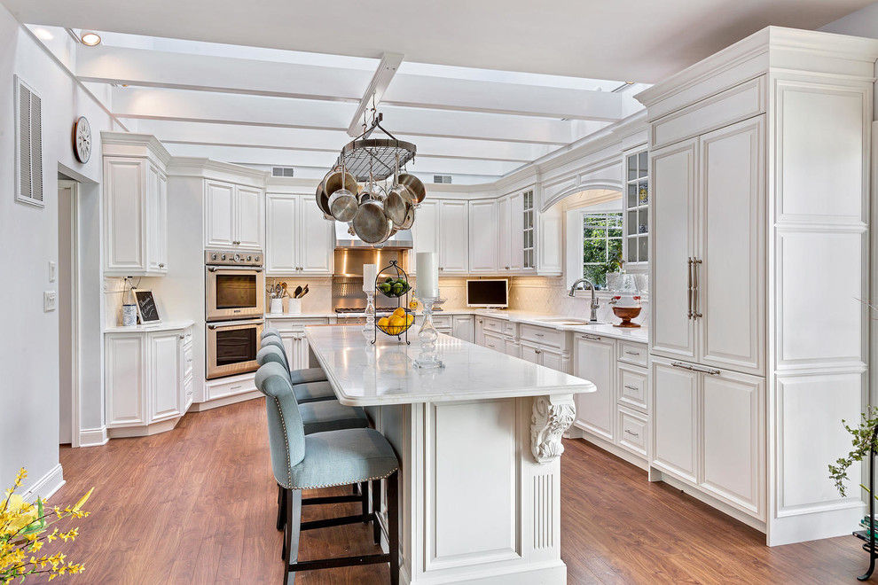 This is an example of a large traditional l-shaped eat-in kitchen in New York with an undermount sink, raised-panel cabinets, white cabinets, marble benchtops, white splashback, medium hardwood floors and with island.