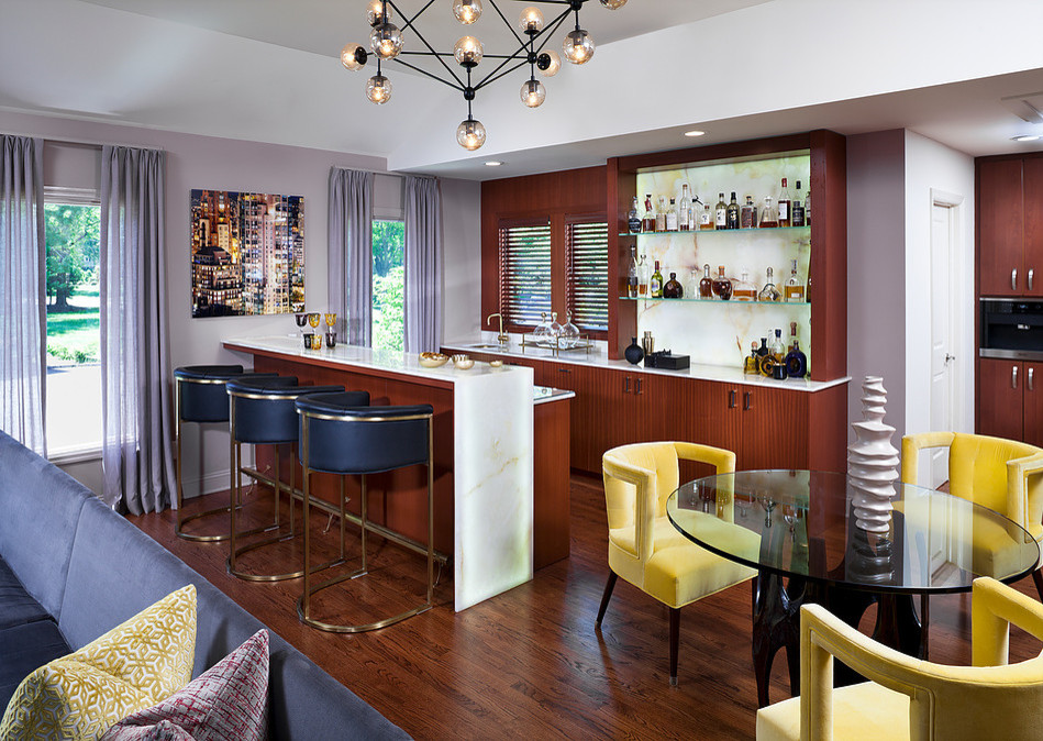 This is an example of a large u-shaped seated home bar in New York with an undermount sink, flat-panel cabinets, medium wood cabinets, onyx benchtops, yellow splashback, stone slab splashback, medium hardwood floors and yellow benchtop.