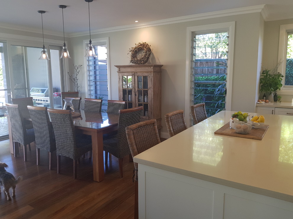 Photo of a small contemporary galley open plan kitchen in Sunshine Coast with a drop-in sink, shaker cabinets, white cabinets, marble benchtops, white splashback, glass sheet splashback, white appliances, bamboo floors, with island, brown floor and beige benchtop.