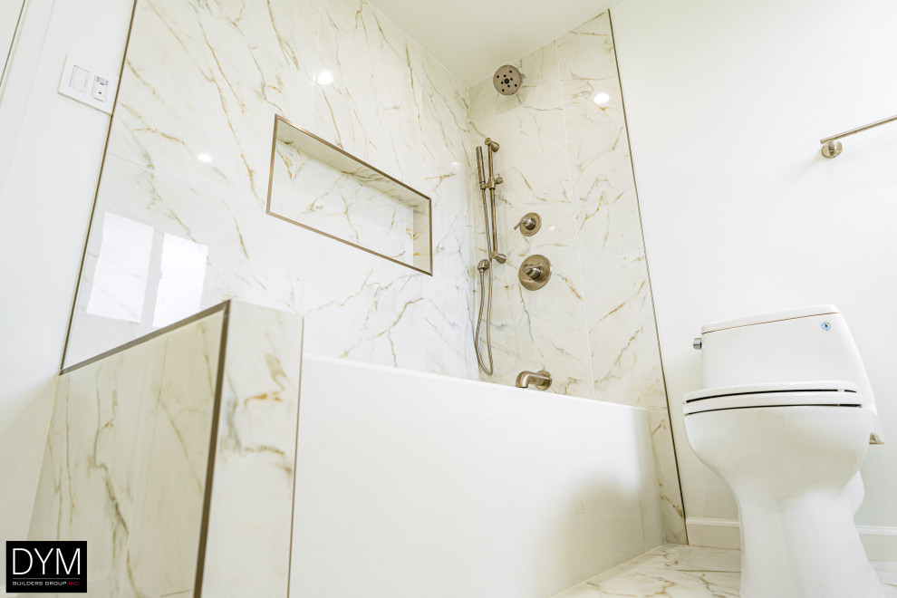 Design ideas for a large modern ensuite bathroom in Orange County with beaded cabinets, white cabinets, a shower/bath combination, a one-piece toilet, white tiles, marble tiles, white walls, marble flooring, a built-in sink, solid surface worktops, white floors, a hinged door, white worktops, a shower bench, double sinks, a built in vanity unit, a wallpapered ceiling and wallpapered walls.